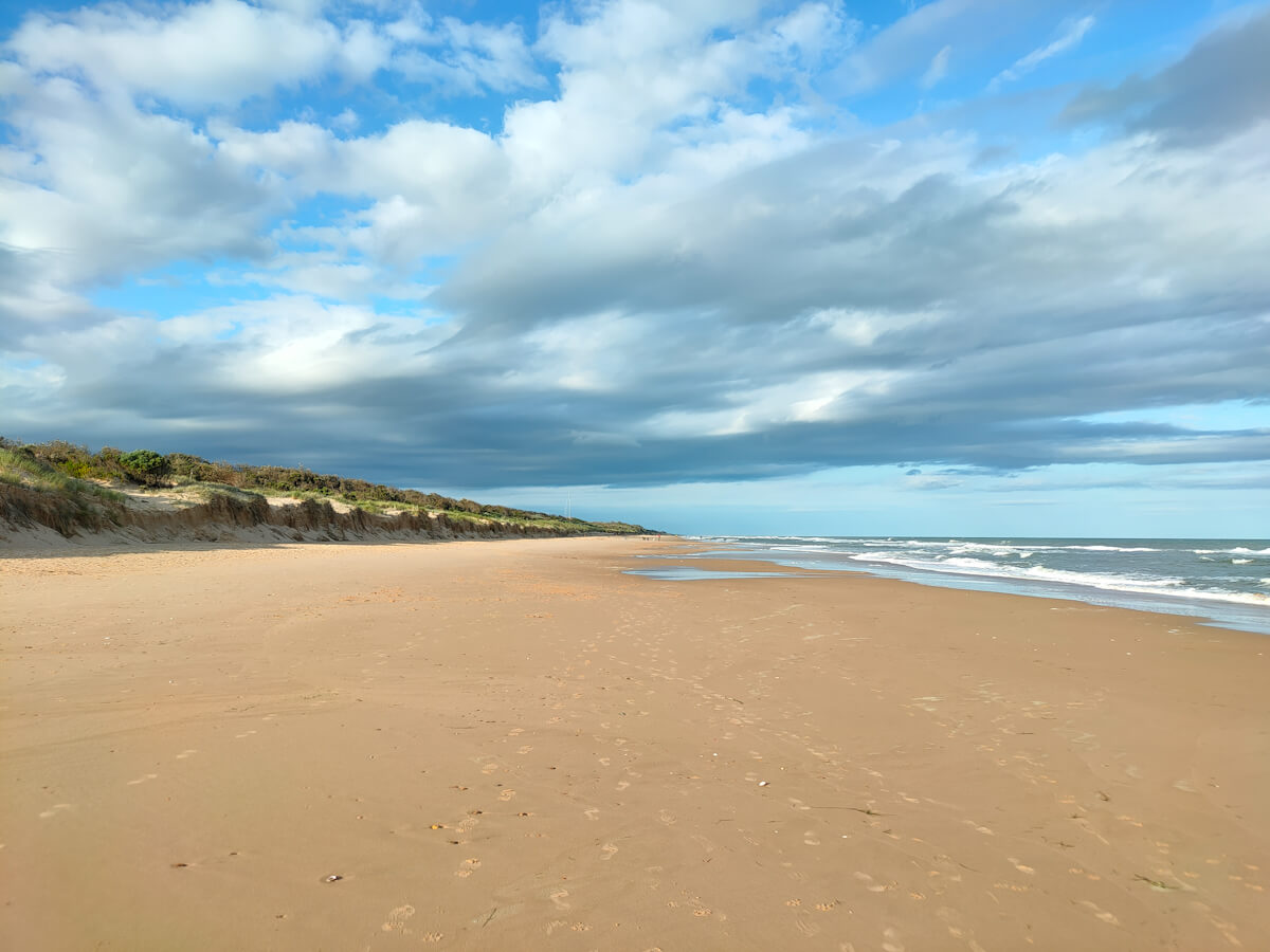 A wide, golden section of 90 mile beach at Seaspray with blue sky and clouds